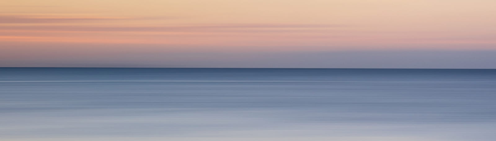 A peaceful seascape during sunset with soft hues of orange, pink, and blue.