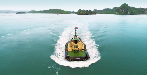A MedTug tugboat navigating through calm waters with lush green islands in the background.