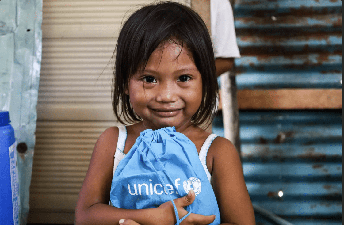 A young child holding a UNICEF-branded drawstring bag while smiling. ©UNICEF Philippines